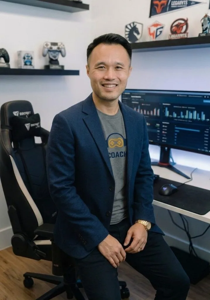 Chris Tran at his gaming setup, wearing a coach shirt with esports memorabilia on the shelves behind him